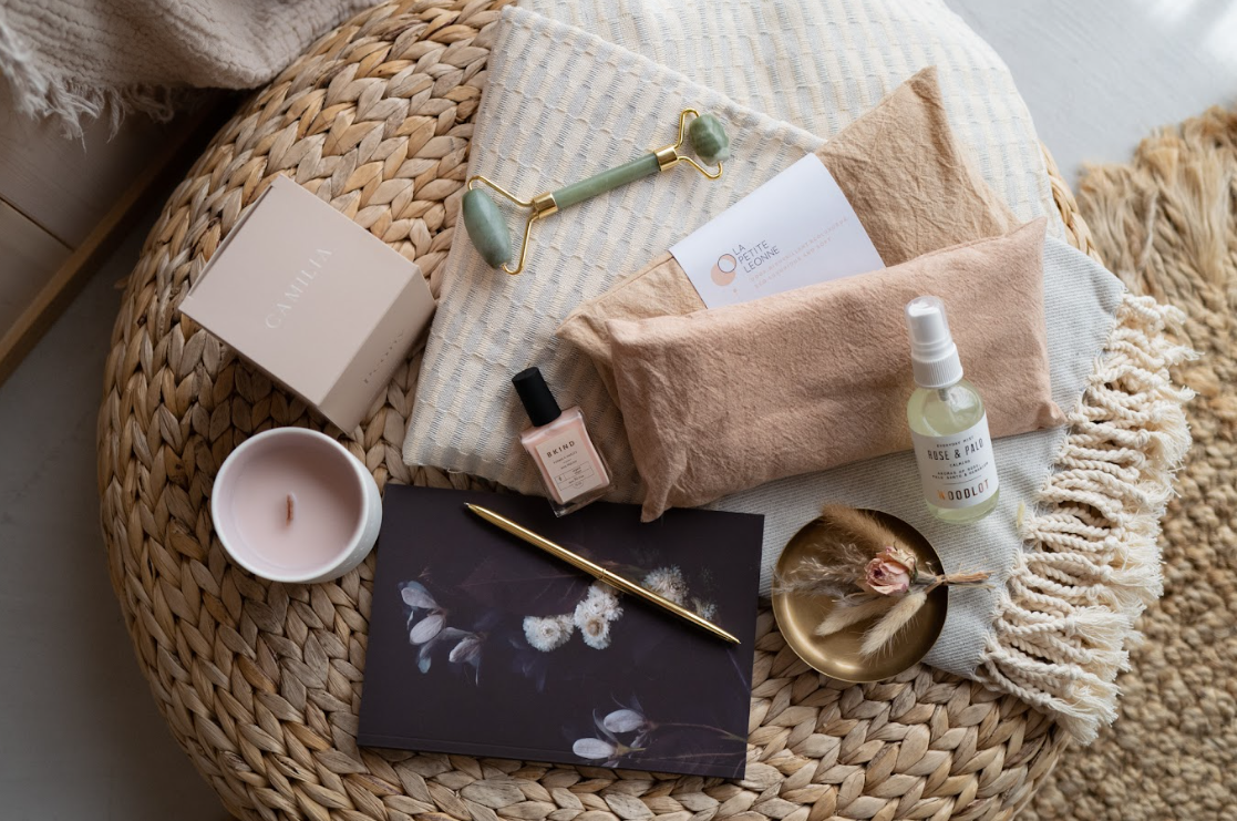 Fall self-care essentials including candle, facial mist, jade roller, and cozy blanket styled on a woven tray