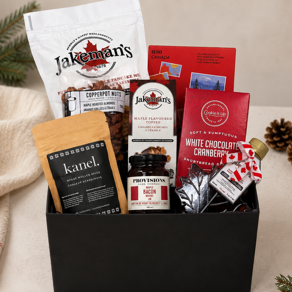 A curated gift basket in a black rectangular box containing Jakeman's pancake mix, chocolate, and candy items, alongside Kanel mulled spice mix, and other Canadian maple flavoured food items.